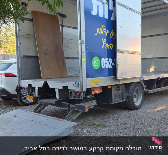 משאית פתוחה עם רמפה בחניה ליד עץ